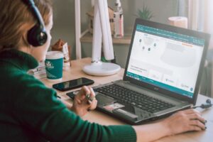 Virtuelle Assistentin mit Kopfhörern arbeitet am Schreibtisch mit Laptop und Notizen