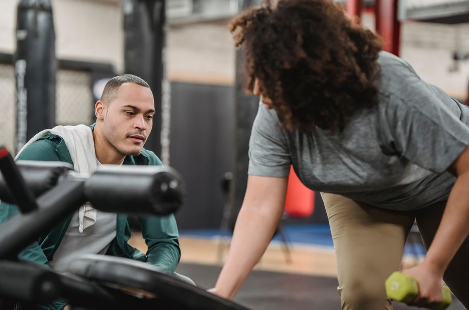 Personal Trainer korrigiert eine Kundin bei einer Kraftübung im Studio